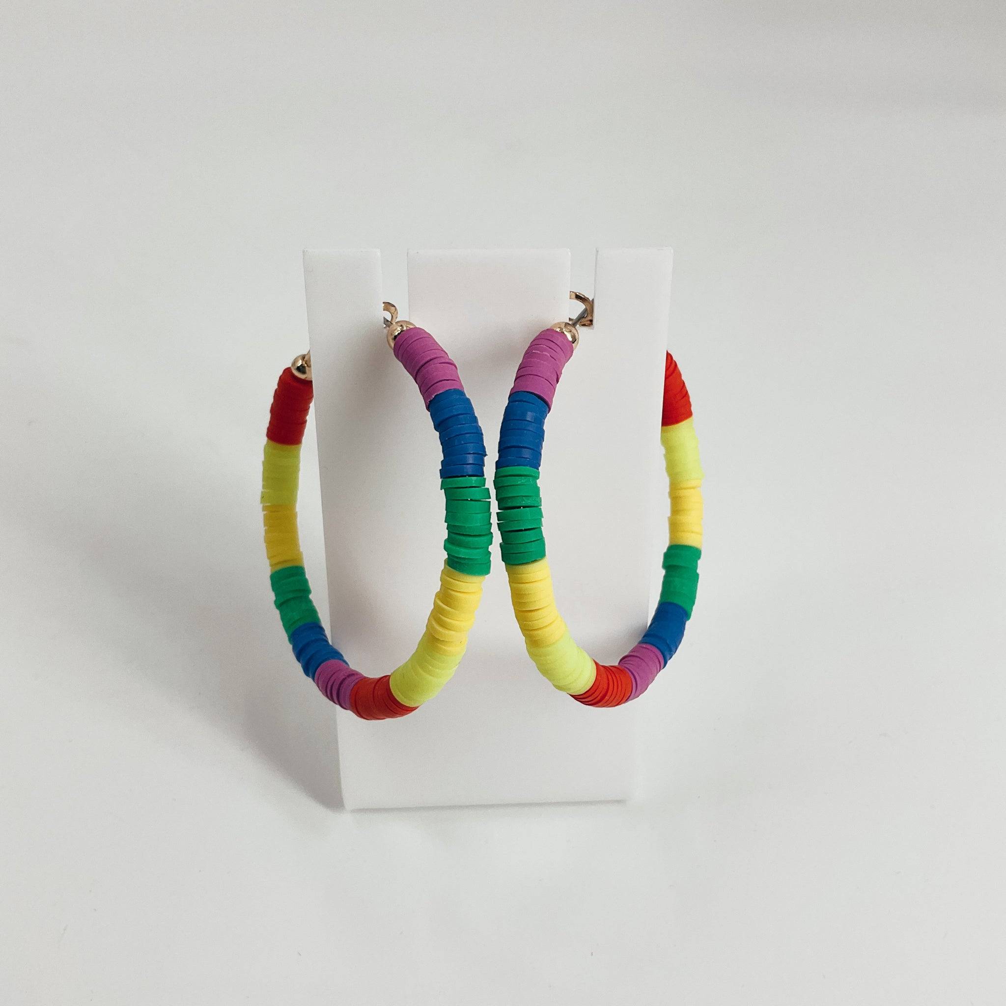 Colorful rainbow hoop earrings made of stacked polymer clay discs, displayed on a white stand. Earrings ideal for bold, vibrant fashion statements.