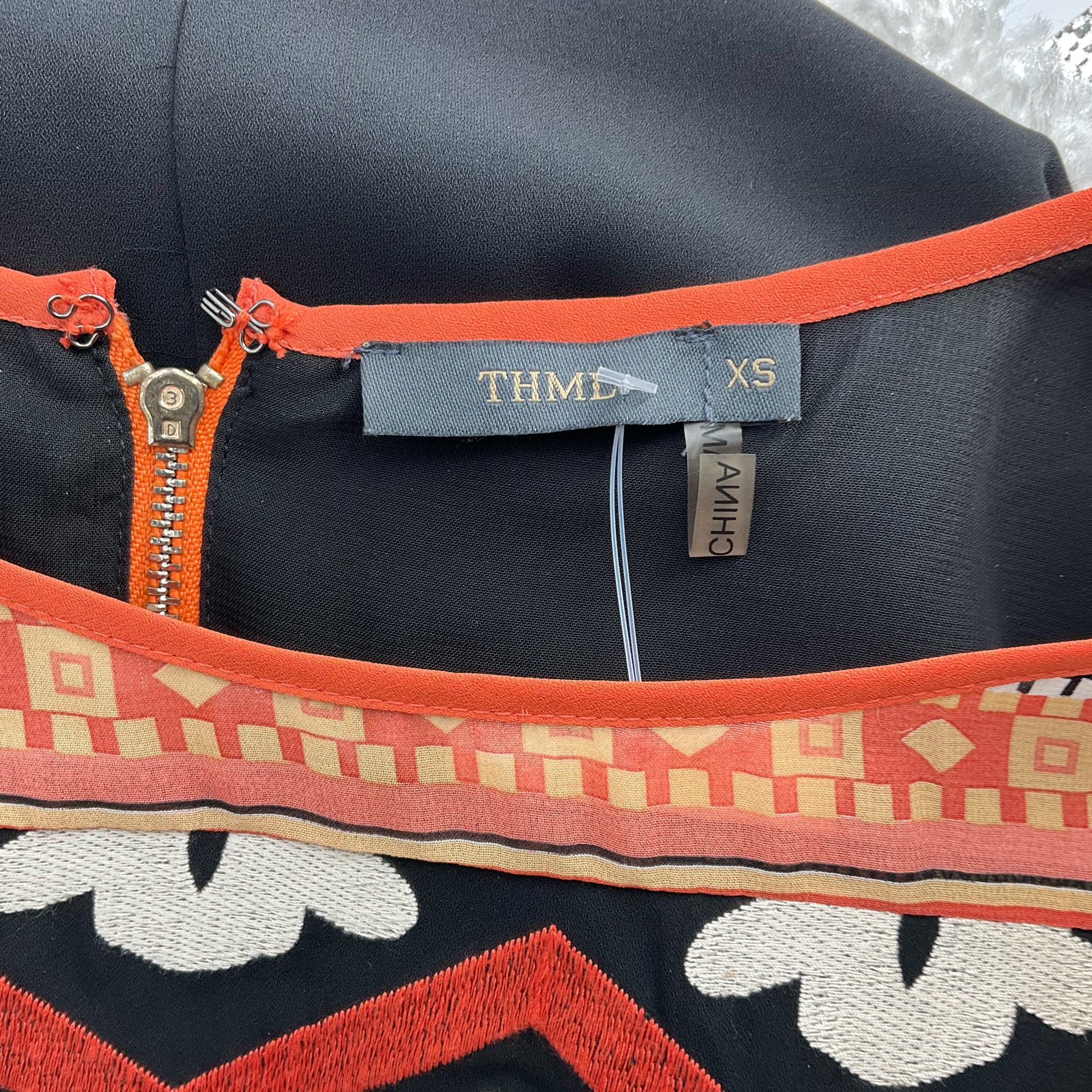 Close-up of THML brand label and size XS tag on Coral/Multi Aztec Dress, highlighting neckline and zipper stitching.