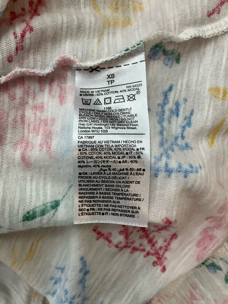 Close-up of fabric tag on Gap White/Multi Floral Pre-Owned Ladies Top - Size XS, detailing cotton-modal blend and care instructions.