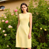 Model wearing Calvin Klein crew neck knee length yellow dress, size 12, surrounded by blooming flowers at Margaret’s Fine Consignments.