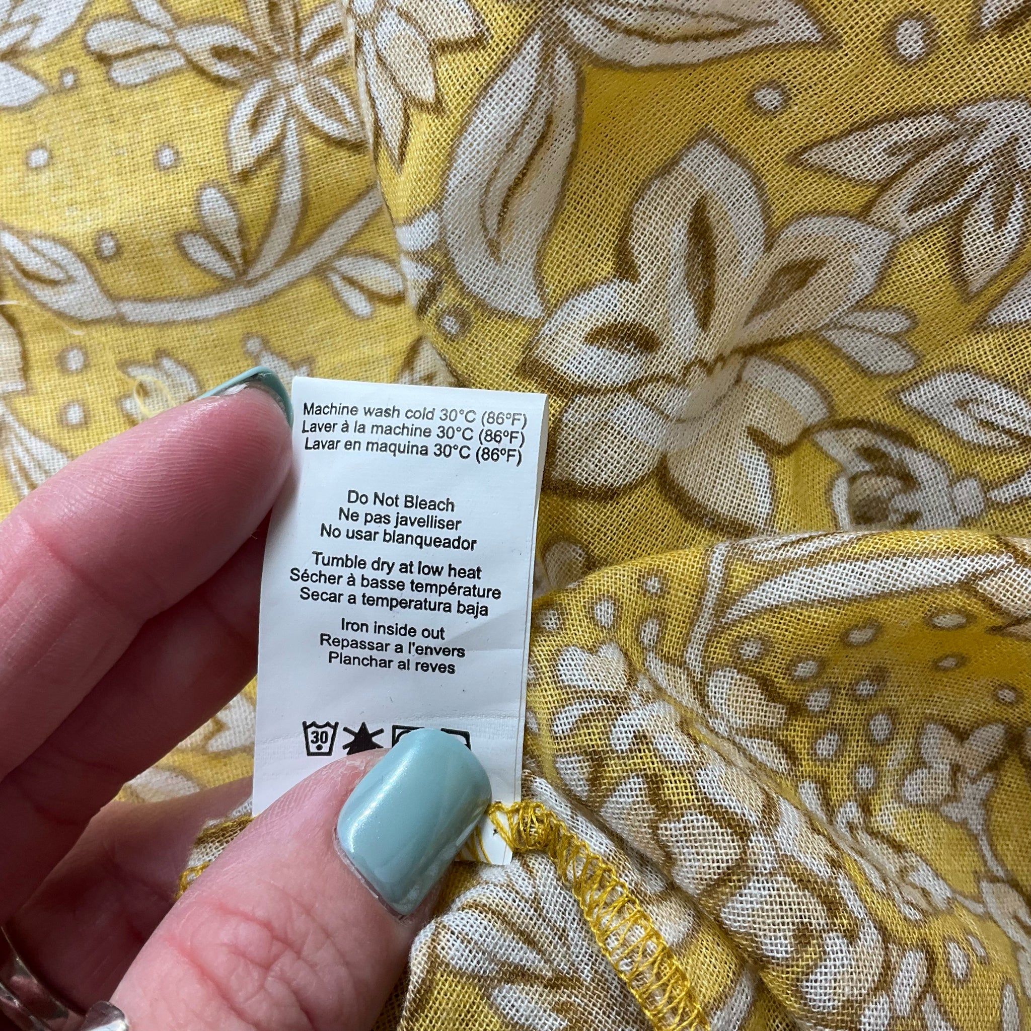 Care label of Sundry Yellow/Tan Floral Dress - Size 4 with washing instructions, ensuring proper maintenance of this pre-owned cotton dress.