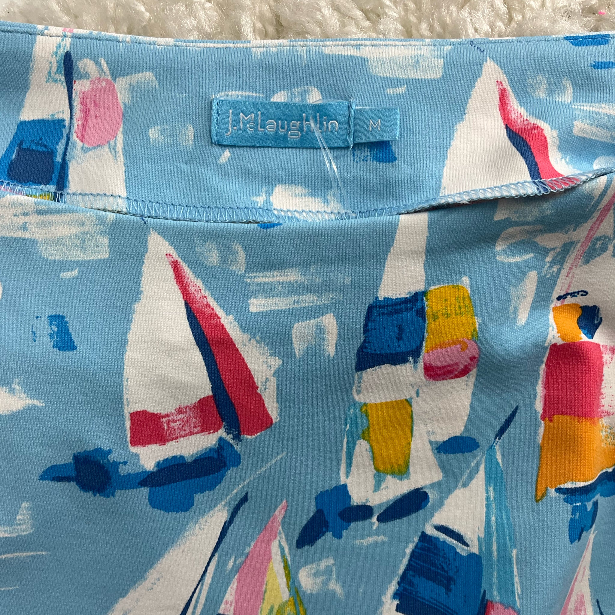 Close-up of J Mclaughlin label on Blue/Multi Sailboats Top - Size Medium, showcasing brand authenticity and vibrant sailboat design.