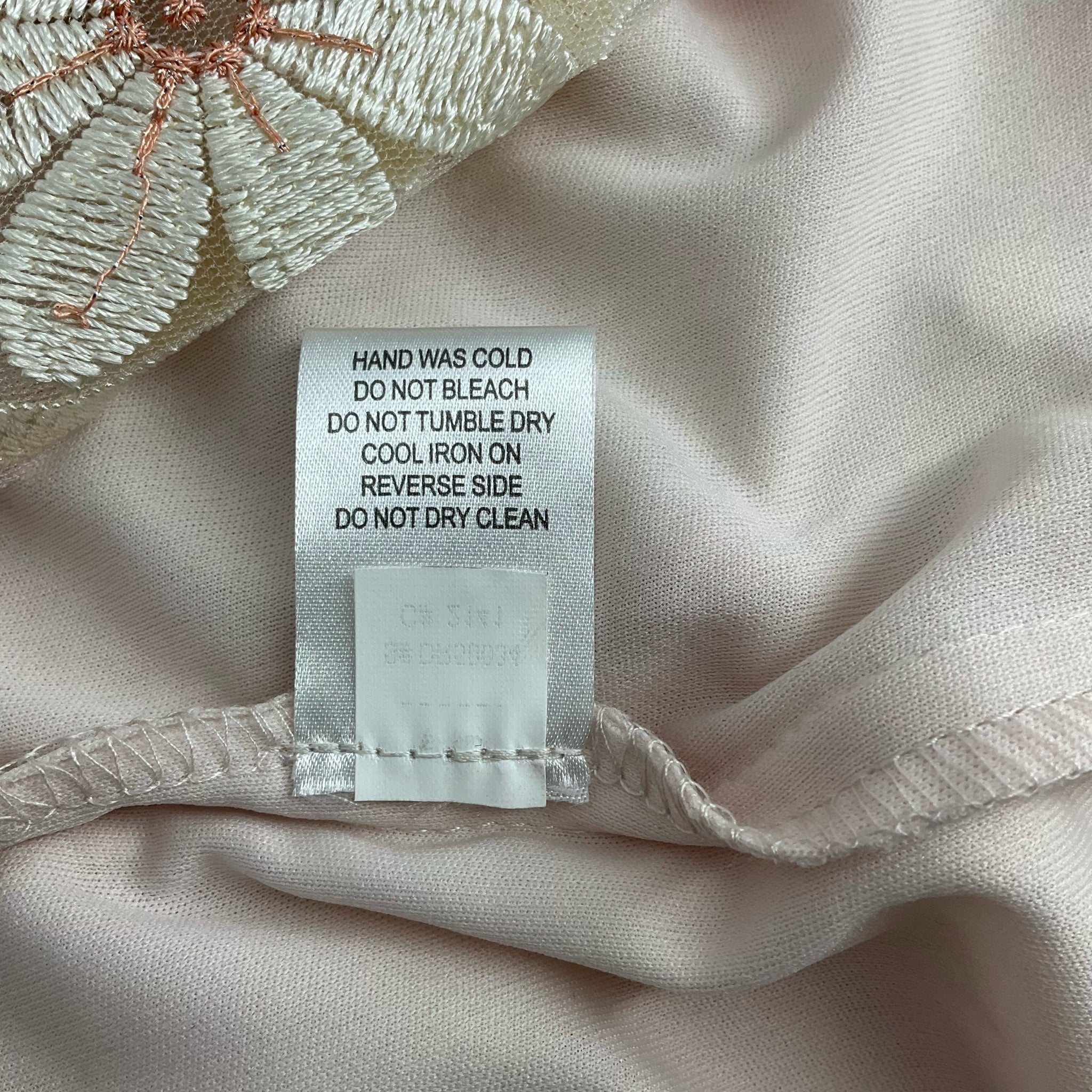 Duplicate care label for Donna Ricco Peach/Cream Floral Dress - Size 10, emphasizing gentle wash and ironing instructions.