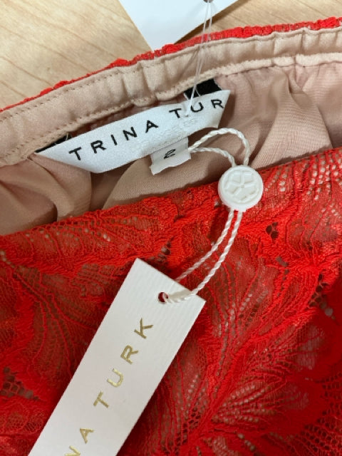 Brand tag and size label of Trina Turk orangish/red lace dress, showing original tags attached. New with tags, size 2.