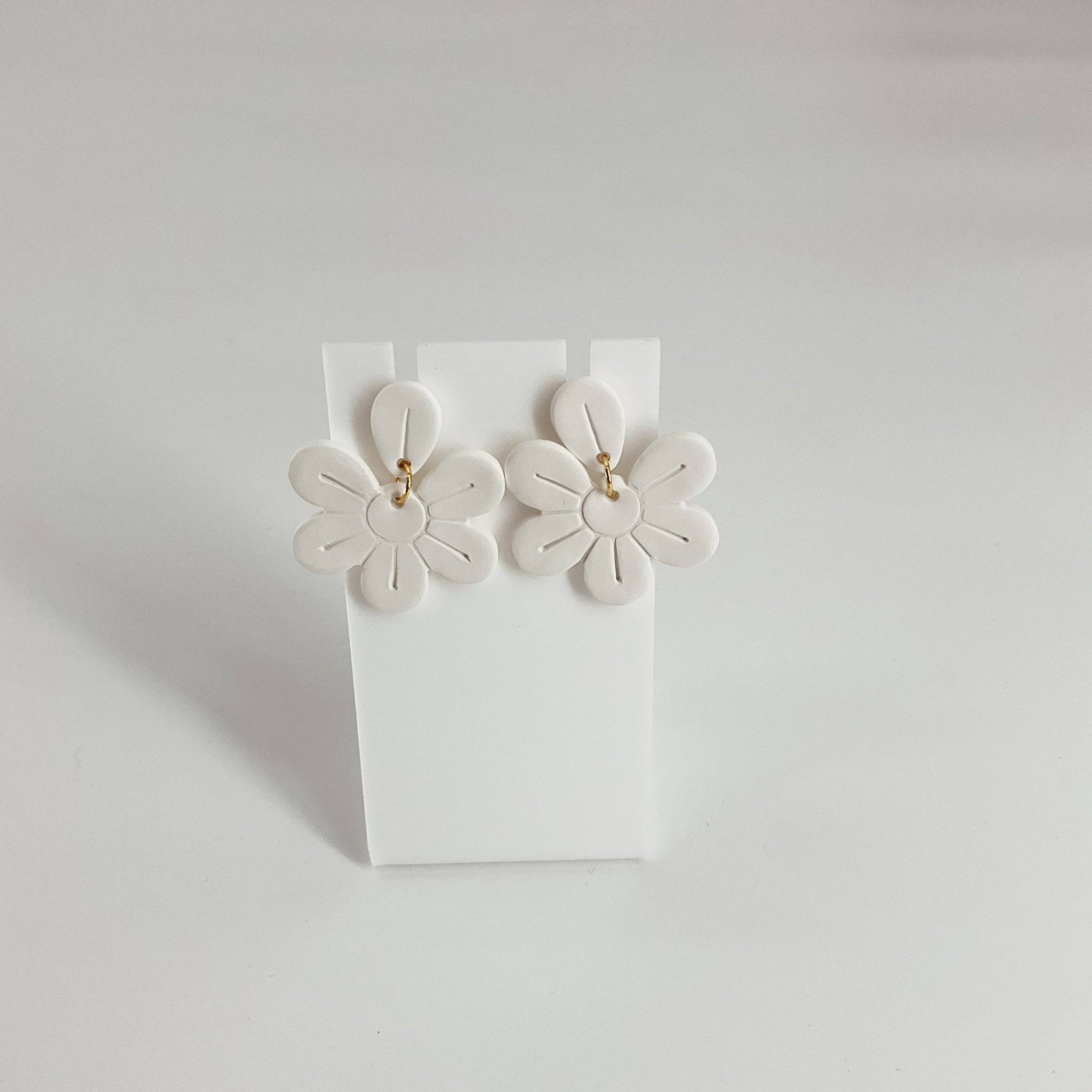 White flower earrings with gold hooks displayed on a white stand, featuring petal-shaped design ideal for floral-themed accessories.