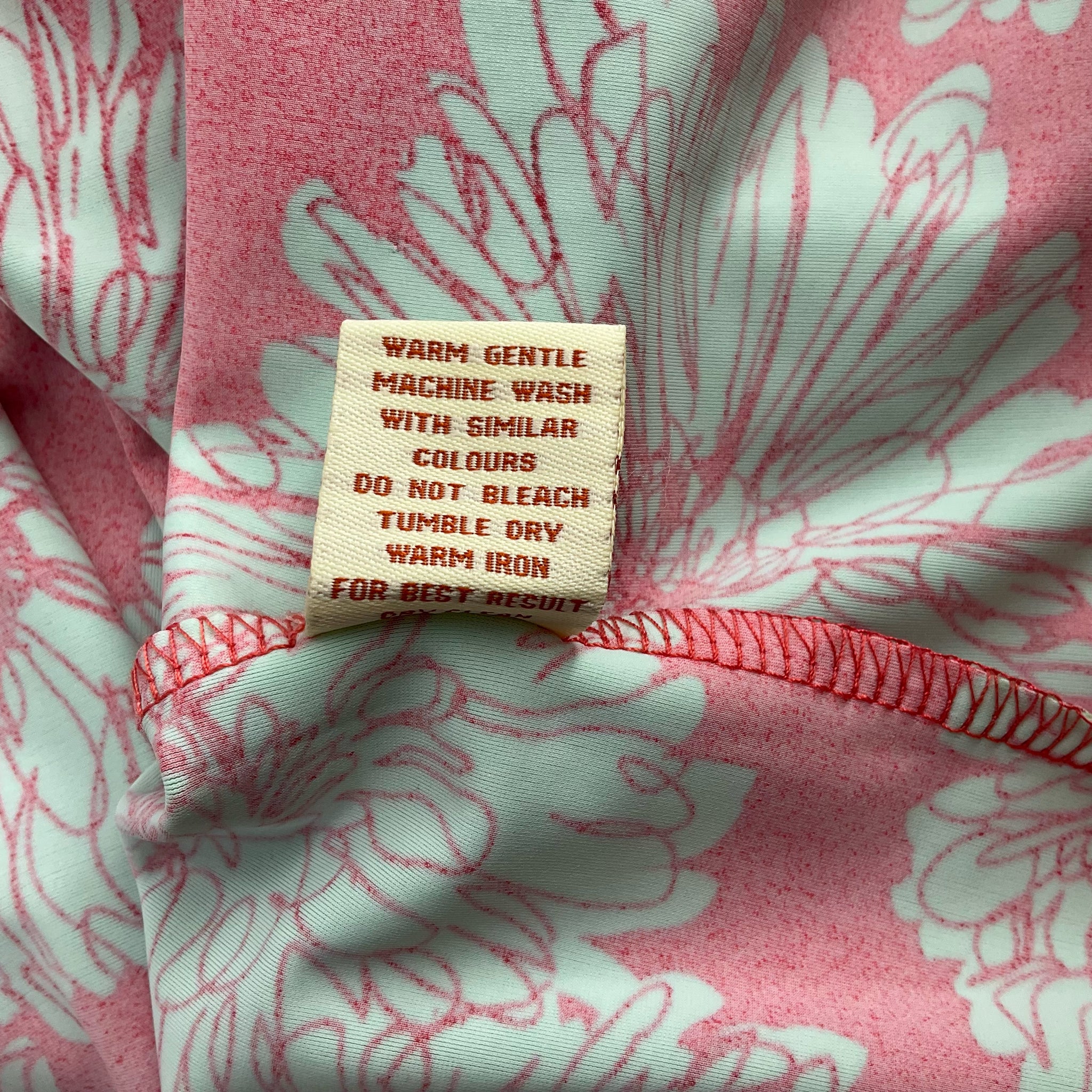 Care label on Aryeh Coral/Green Print Dress - Size Large detailing wash instructions for long-lasting wear.
