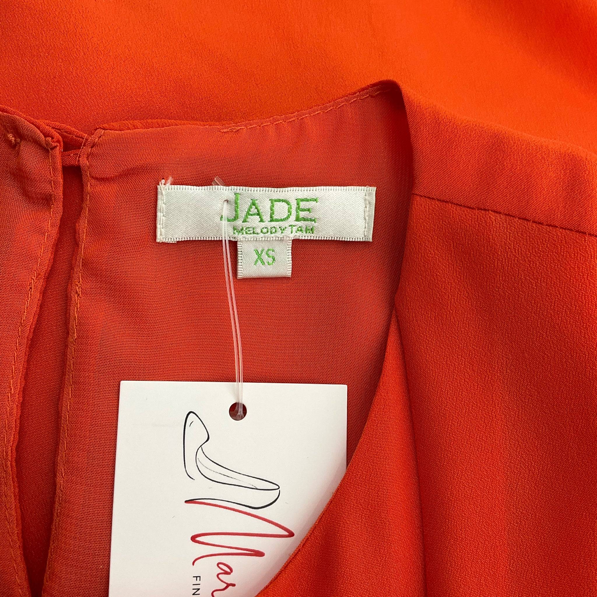 Close-up of Jade brand label and size tag on orange ruffle dress, confirming XS sizing and designer Melody Tam branding.