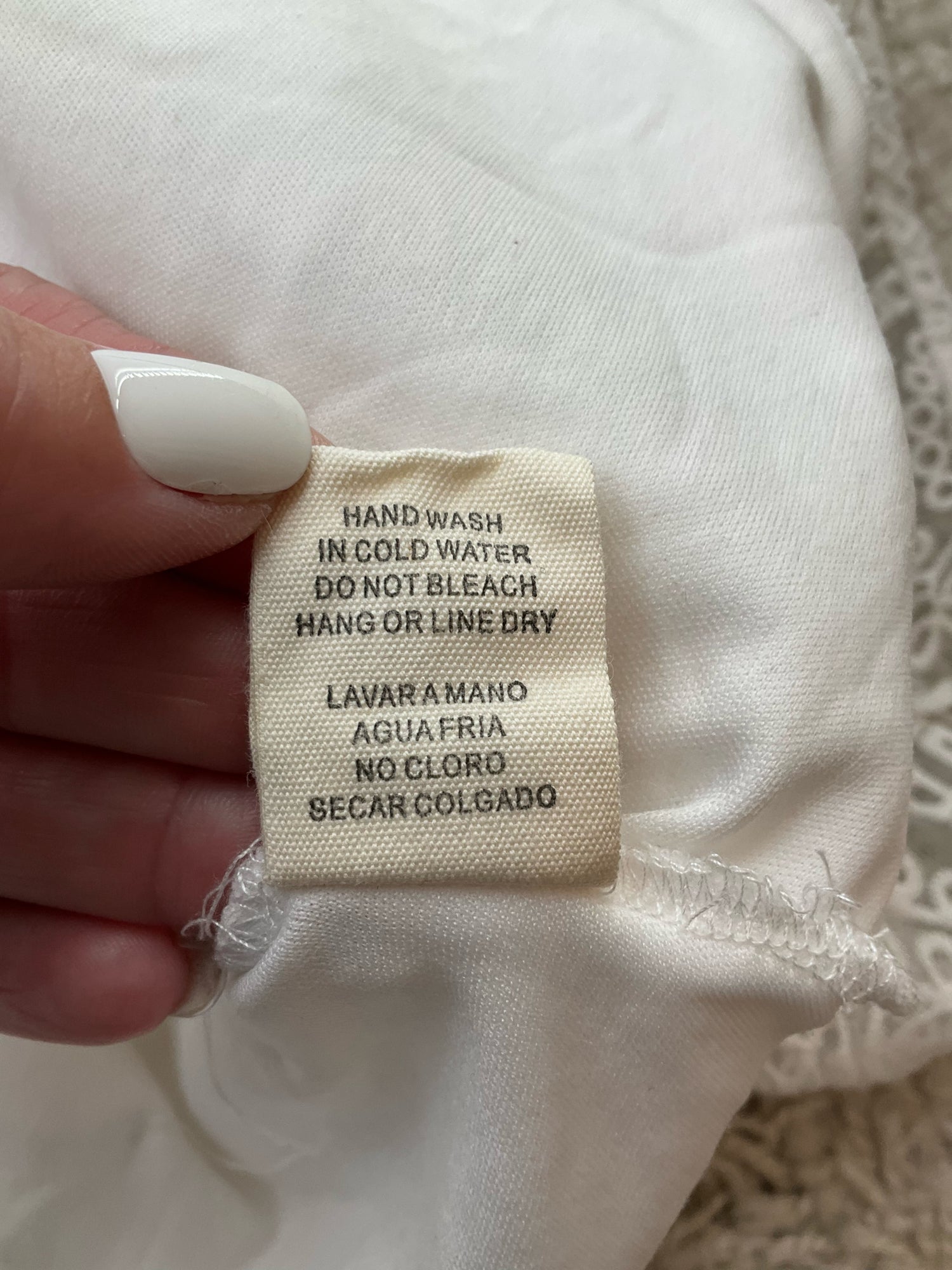 Care label of Illa Illa white lace skater dress with hand wash instructions in English and Spanish, suitable for delicate garment care.