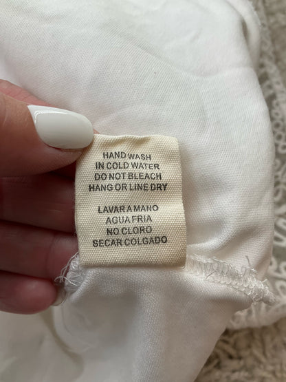 Care label of Illa Illa white lace skater dress with hand wash instructions in English and Spanish, suitable for delicate garment care.