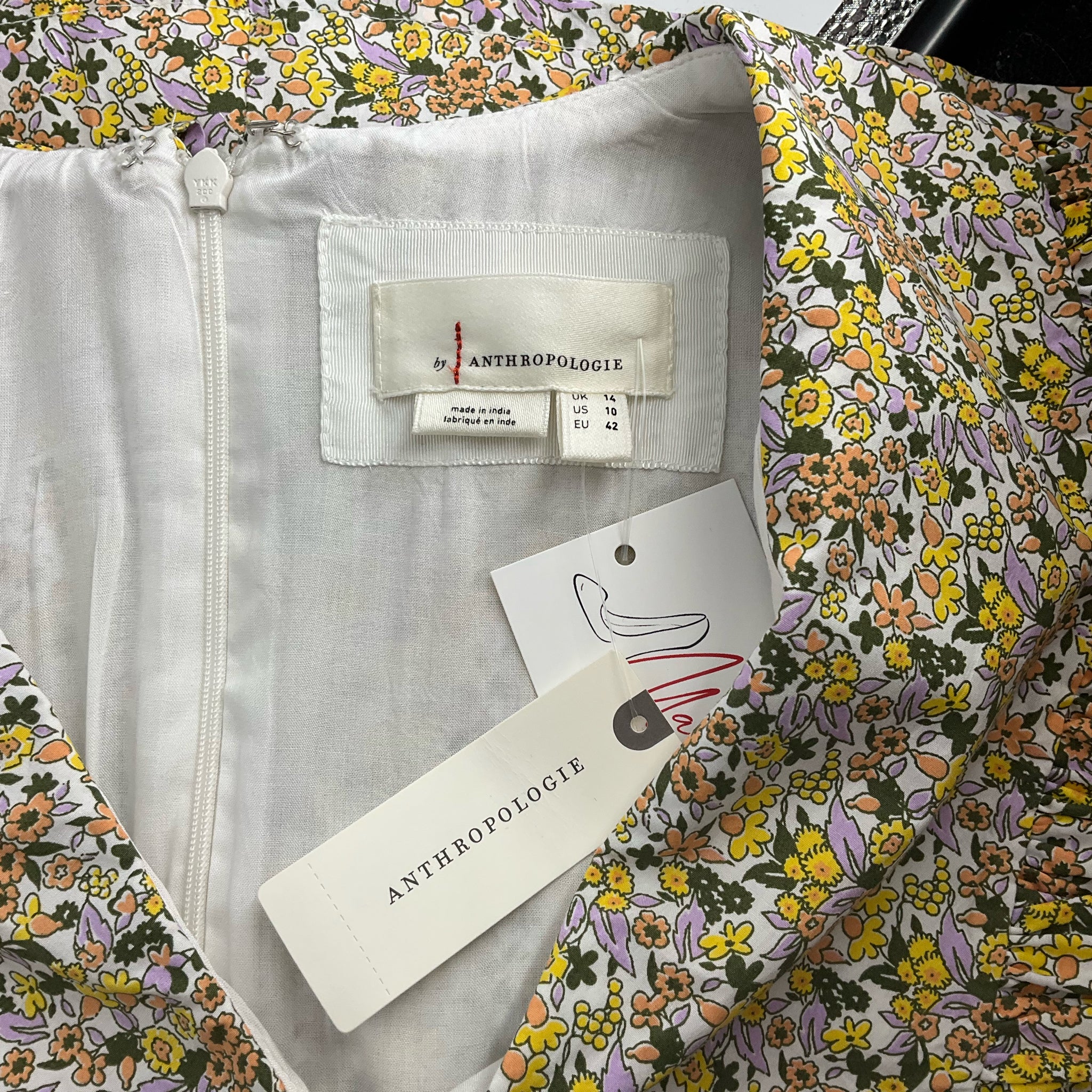 Close-up of Anthropologie label and size tag on Cream/Yellow/Orange Floral Dress - Size 10, marked as new with tags.