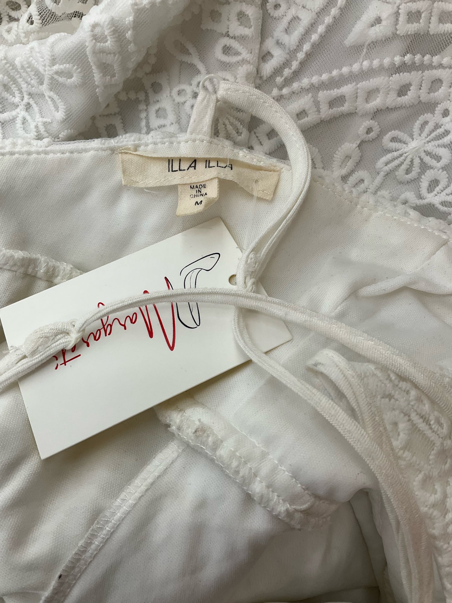 Close-up of Illa Illa dress label showing brand tag and size medium, confirming authenticity of pre-owned white lace skater dress.