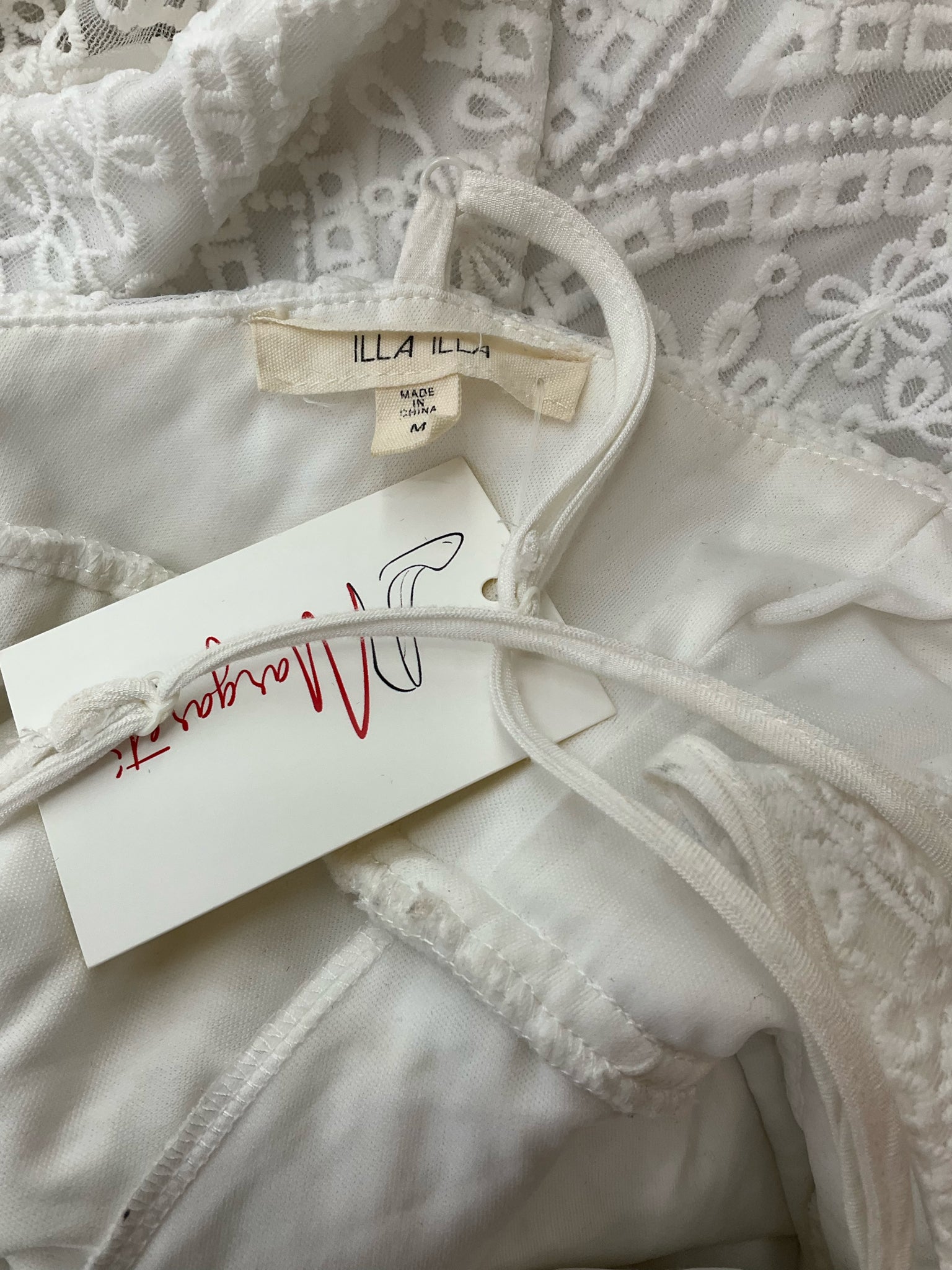 Close-up of Illa Illa dress label showing brand tag and size medium, confirming authenticity of pre-owned white lace skater dress.