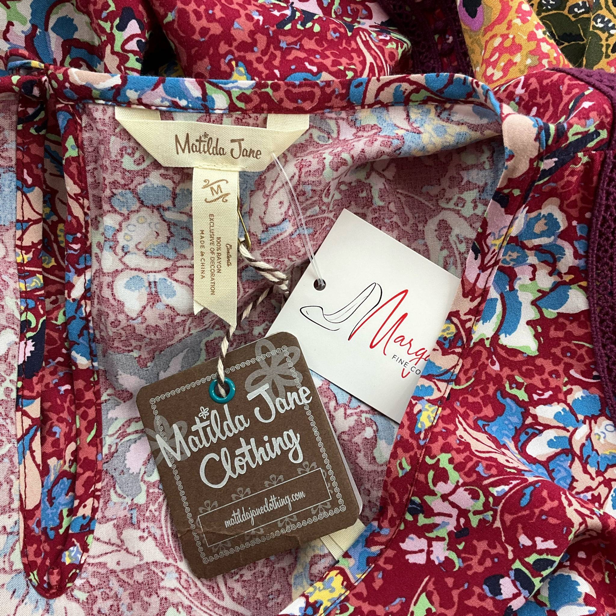 Close-up of Matilda Jane Clothing tags on maroon floral mini dress, size medium, new with tags. Shop sustainable fashion at Margaret’s Fine Consignments.