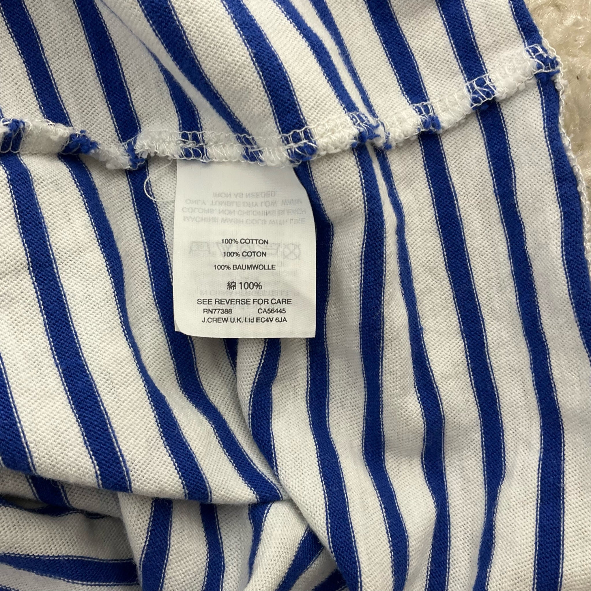 Fabric tag of J Crew White/Blue Stripe Dress - Size Medium, indicating 100% cotton material and care instructions, perfect for summer comfort.