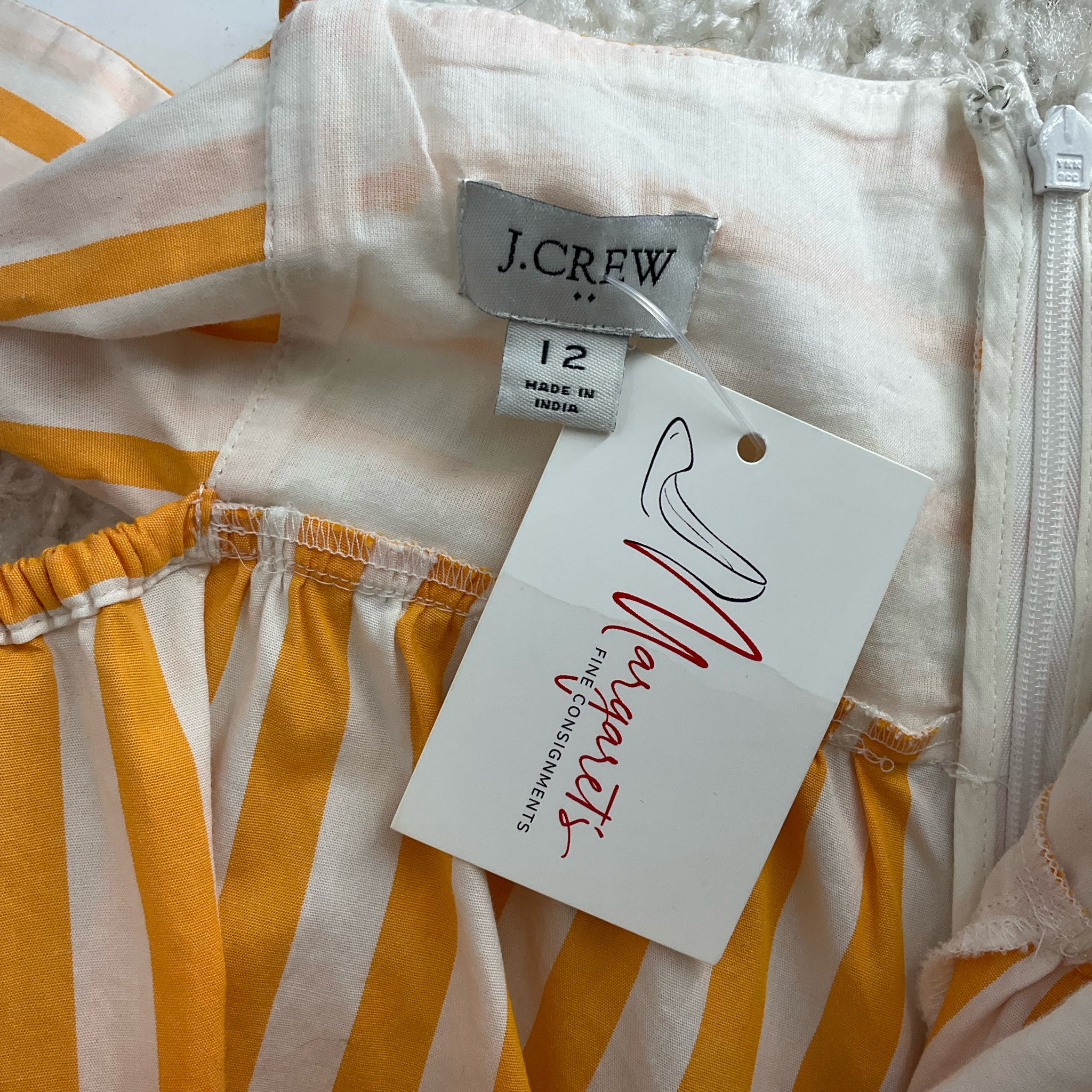 Close-up of J Crew label and Margaret’s Fine Consignments tag on White/Orange Stripe Dress Size 12, confirming pre-owned status.