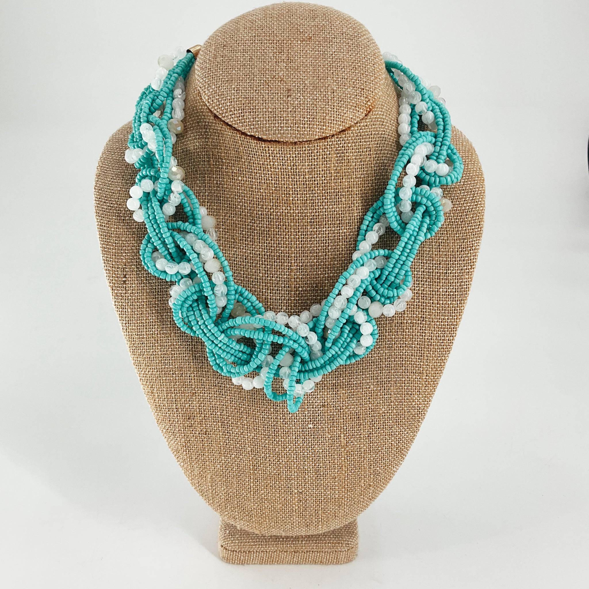 Turquoise/white beaded necklace featuring twisted strands of small turquoise and white beads, displayed on a burlap jewelry bust. Ideal for boho or summer fashion.