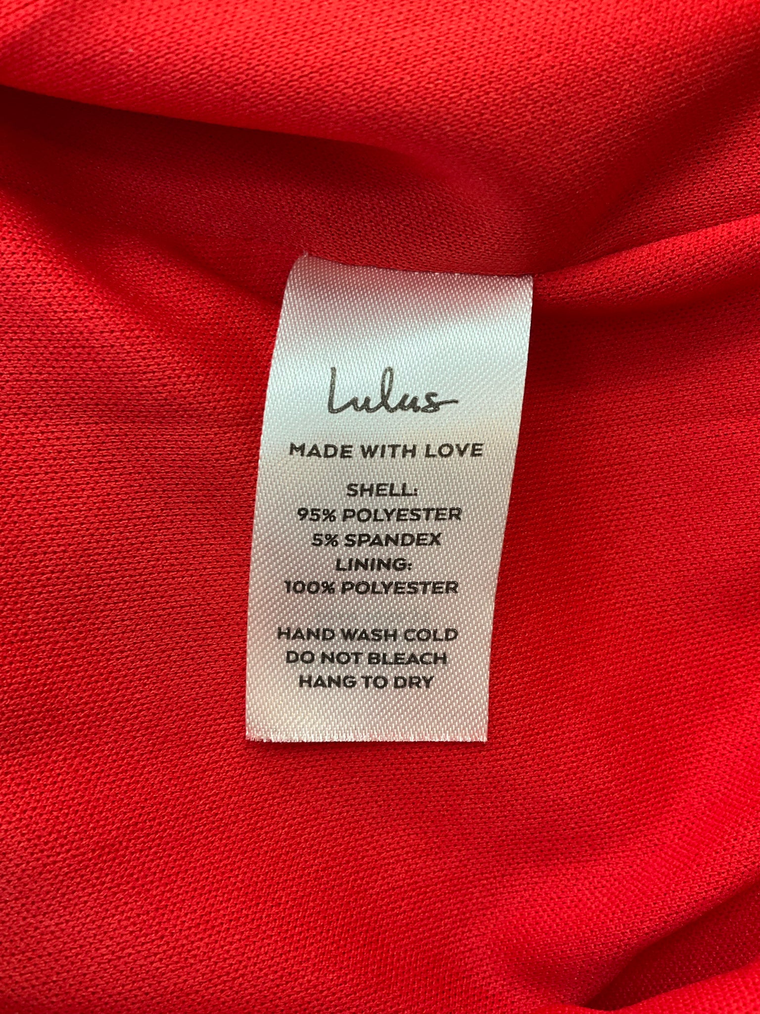 Fabric care label of Lulus Remarkable Presence red dress, detailing polyester-spandex blend and care instructions for this size large cocktail dress.