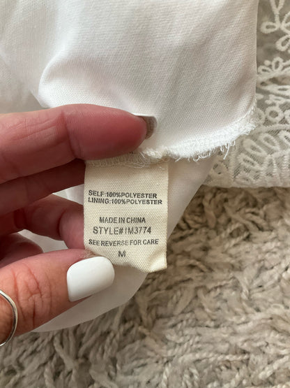 Fabric content tag of Illa Illa white lace dress indicating 100% polyester material and style number IM3774, size medium.