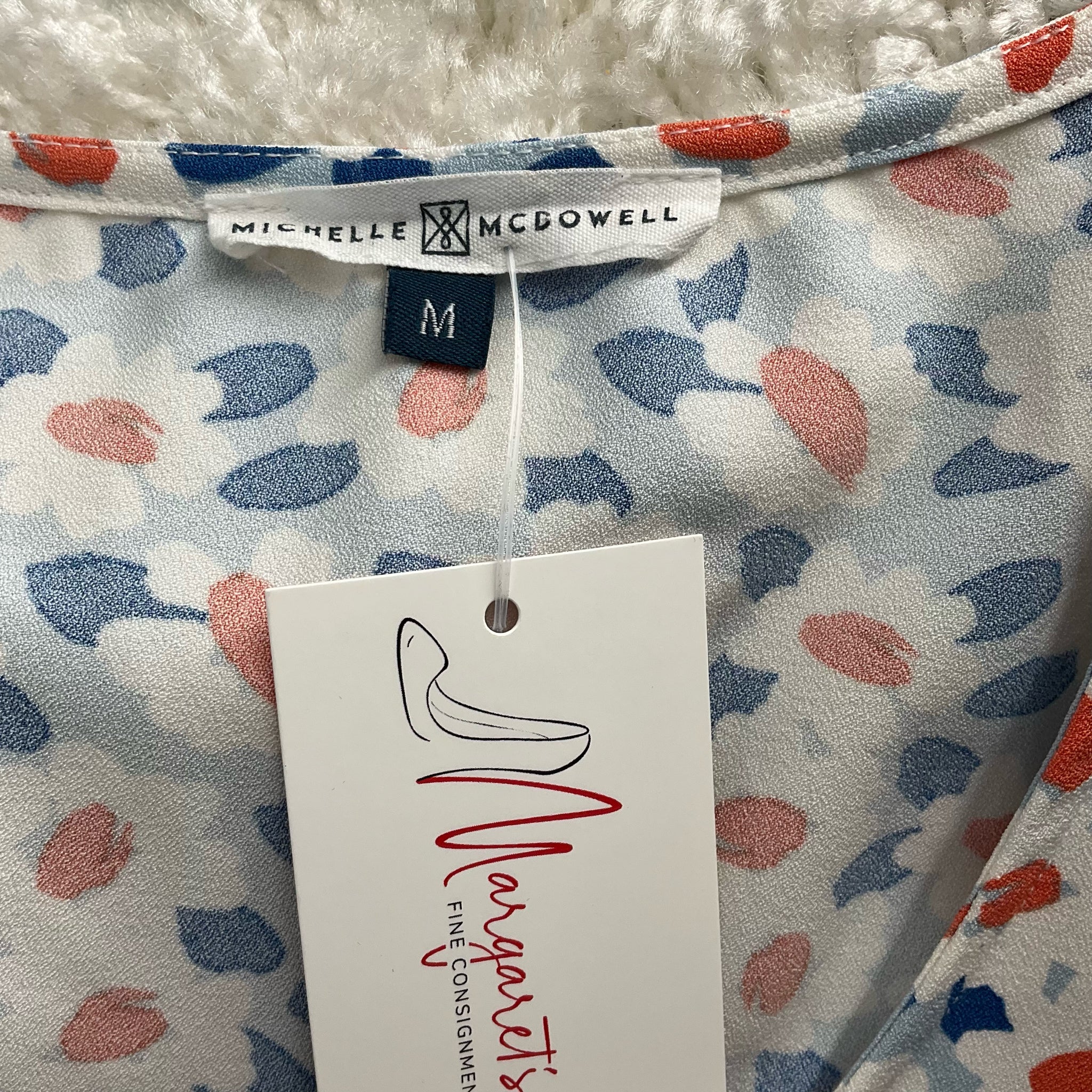 Close-up of Michelle Mcdowell label and size tag on Blue/Orange Floral Top - Size Medium, confirming brand authenticity and pre-owned condition.
