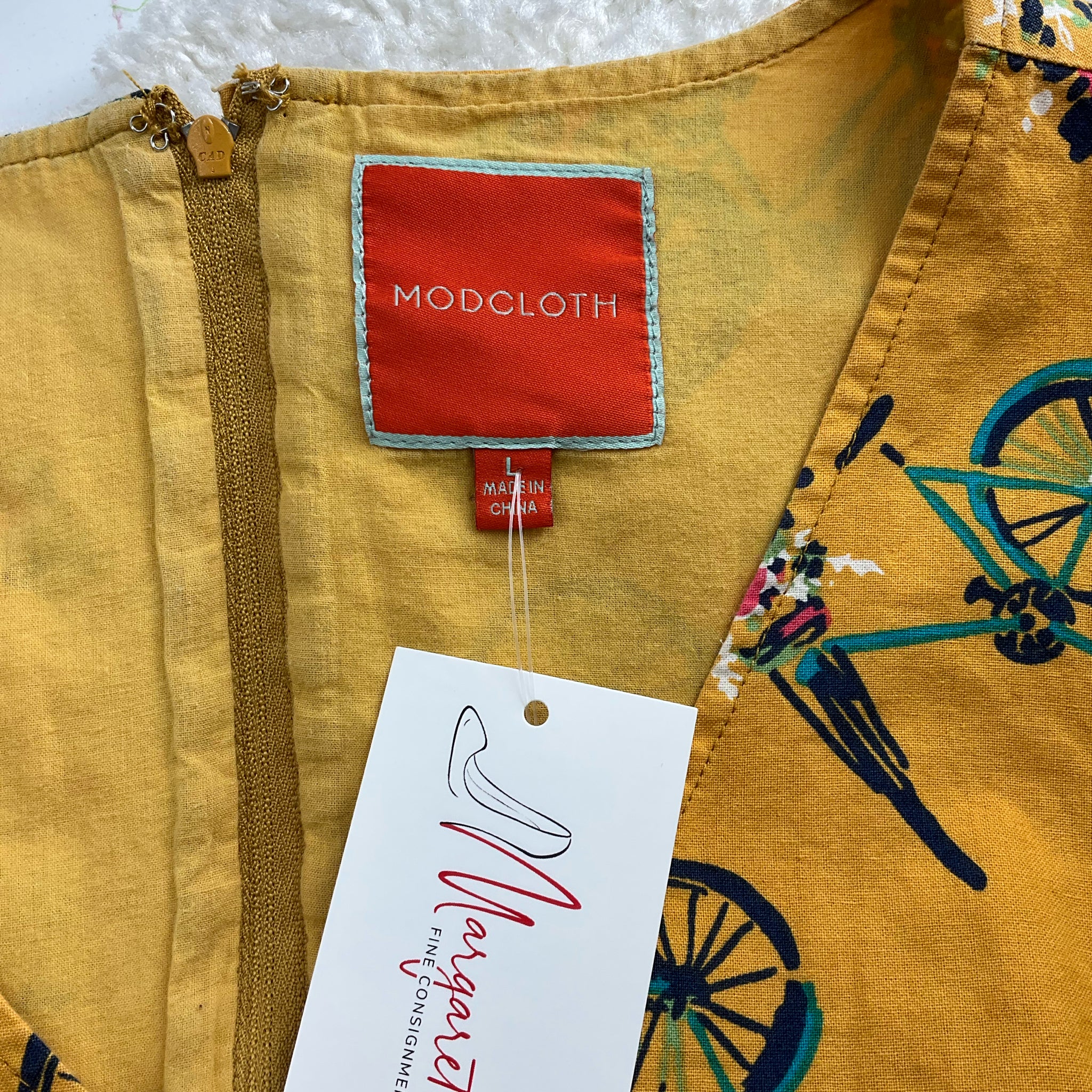 Close-up of Modcloth label and Margaret's Fine Consignments tag on mustard/multi bike dress, confirming authenticity and pre-owned status.